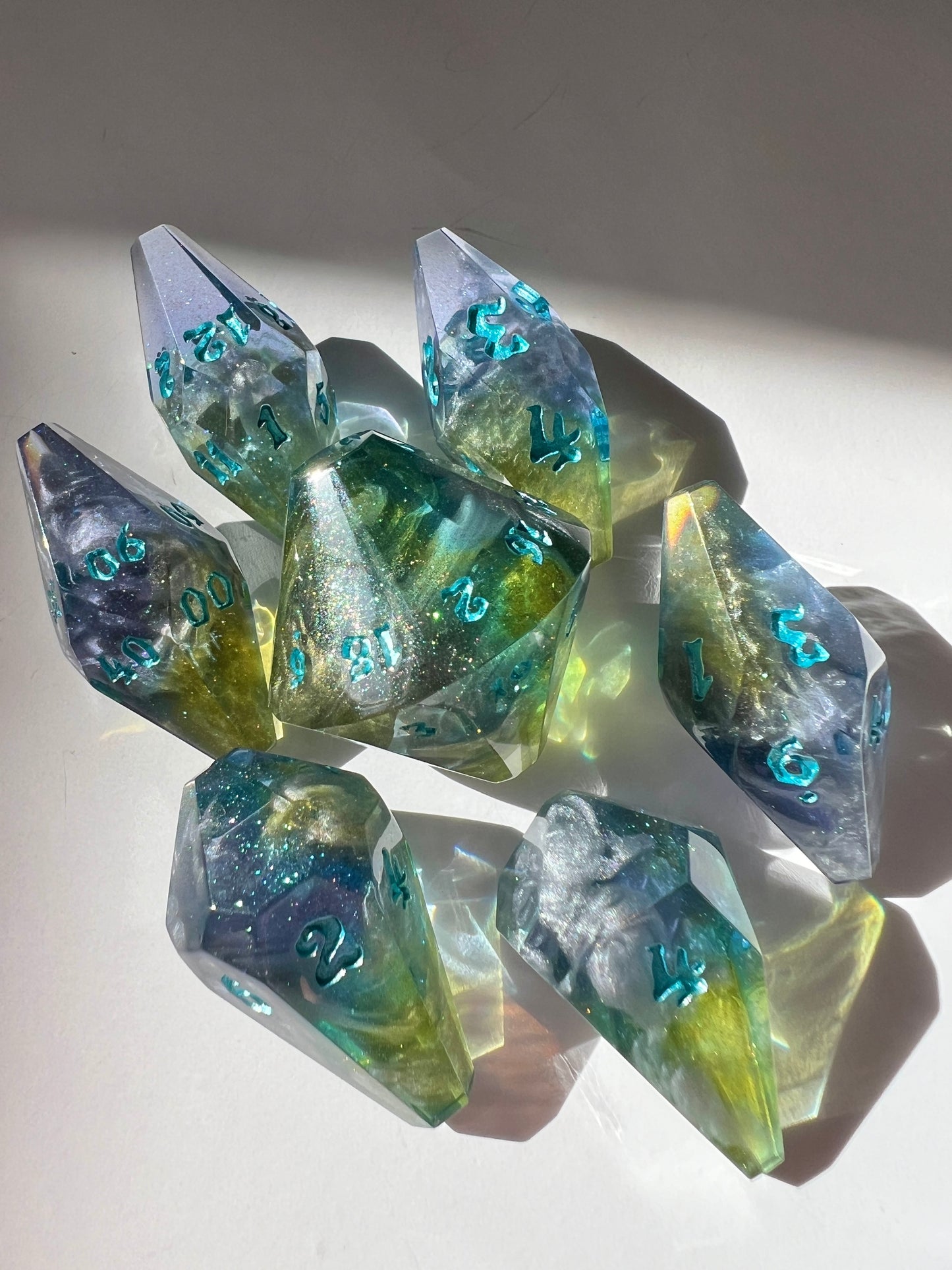 Oversized resin dice with coffin-shaped faces. The dice feature a blue, purple and gold gradient with silver wisps inside.