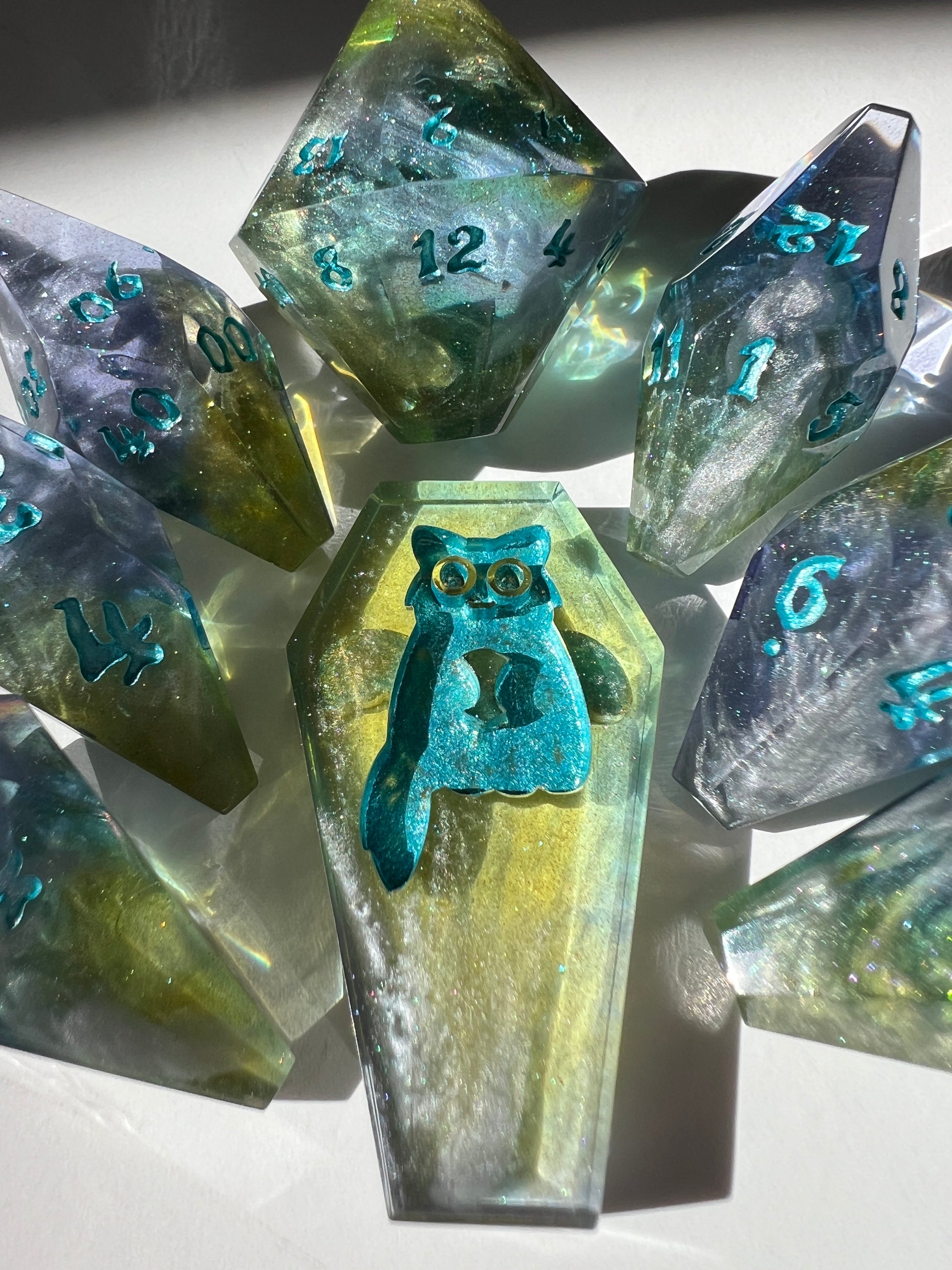 Oversized resin dice with coffin-shaped faces. The dice feature a blue, purple and gold gradient with silver wisps inside.