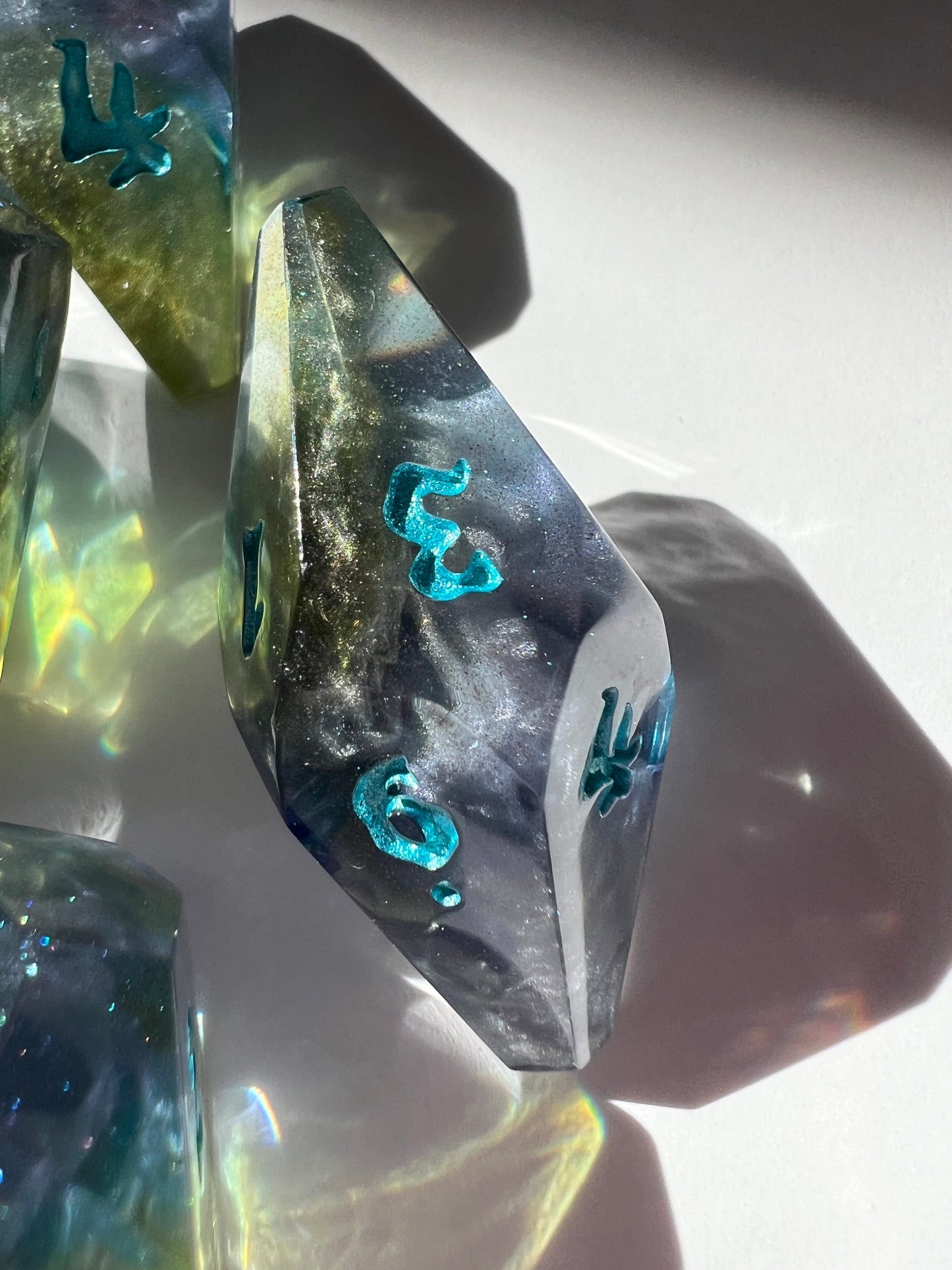 Oversized resin dice with coffin-shaped faces. The dice feature a blue, purple and gold gradient with silver wisps inside.