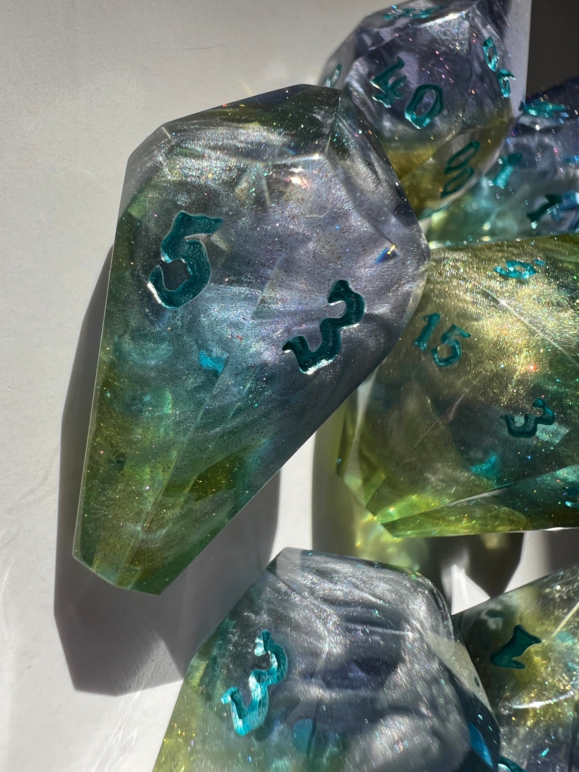 Oversized resin dice with coffin-shaped faces. The dice feature a blue, purple and gold gradient with silver wisps inside.