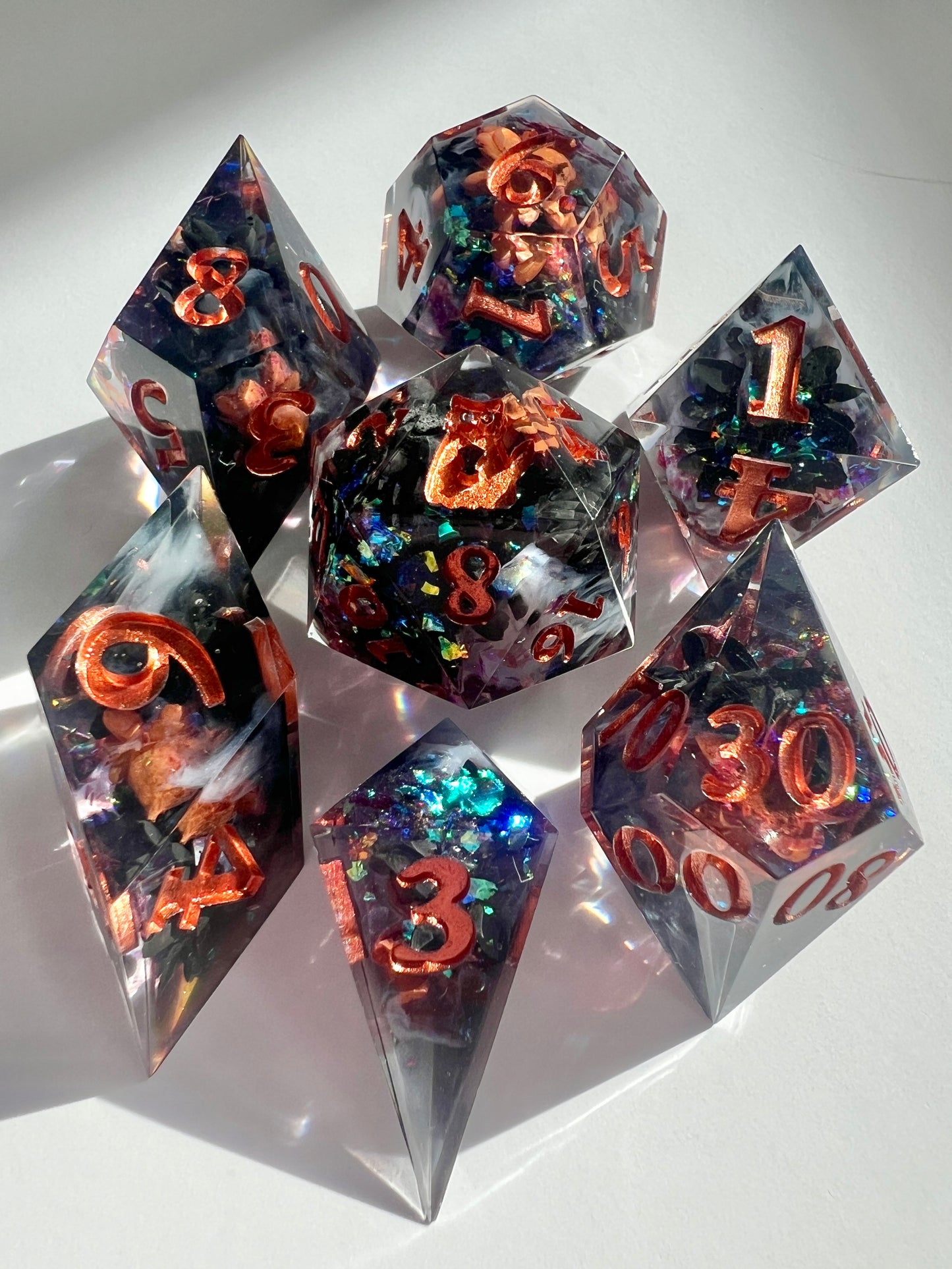 This 7-piece resin dice set includes dried black and orange flowers, holographic flakes and white wisps in a black base.