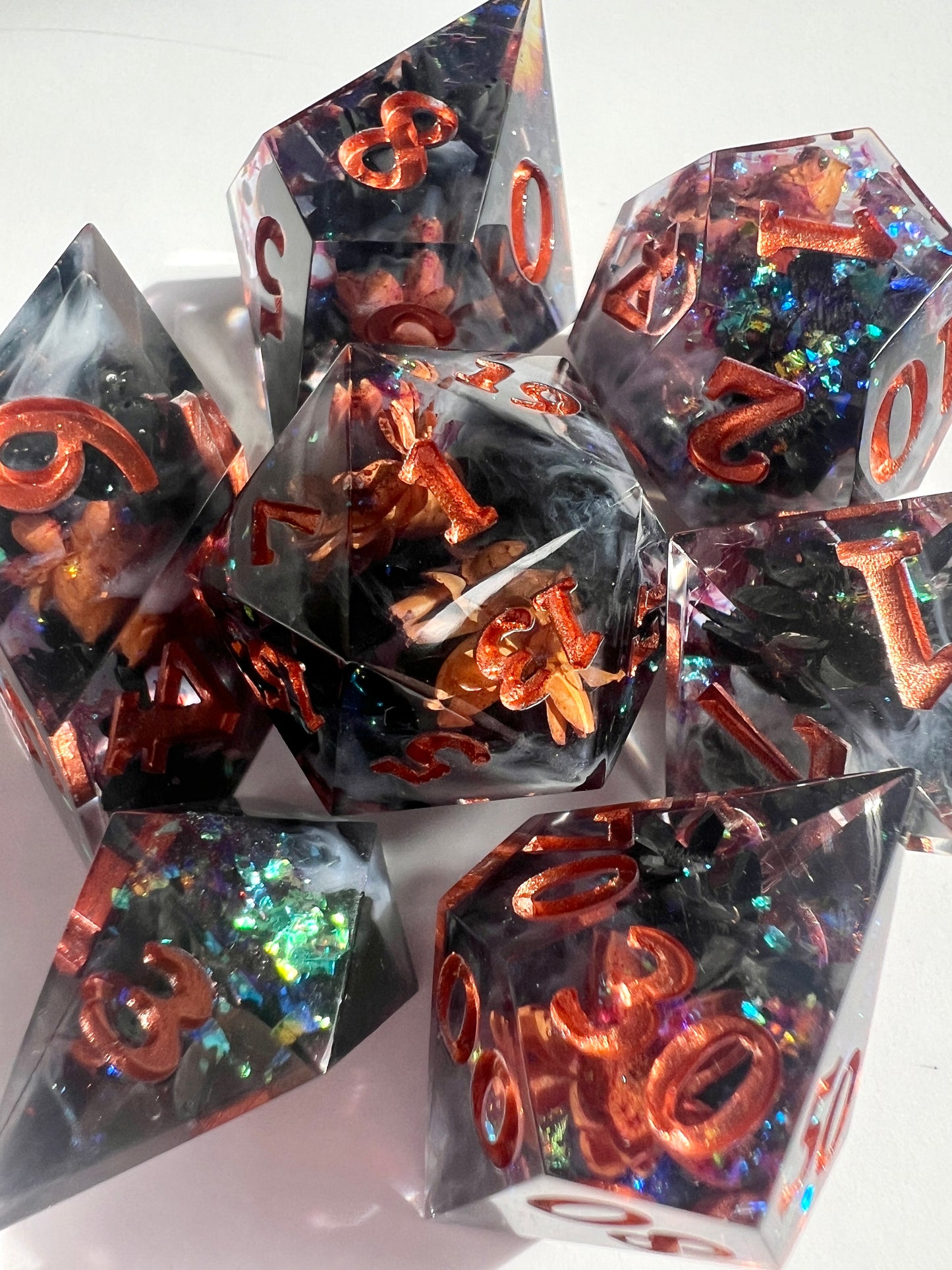 This 7-piece resin dice set includes dried black and orange flowers, holographic flakes and white wisps in a black base.