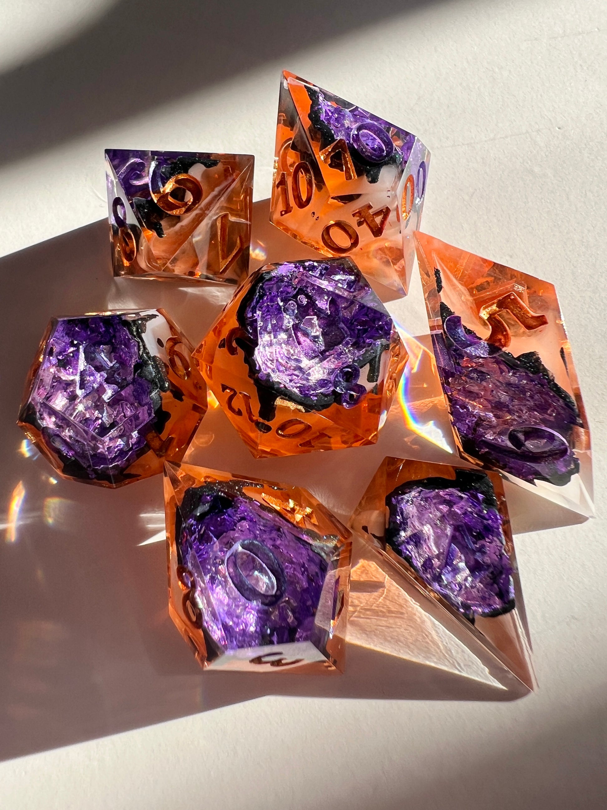 This spooky 7-piece geode-style dice set contains two different shades of purple foil to mimic crystals, a black inky rim, and an orange and cream-colored base.