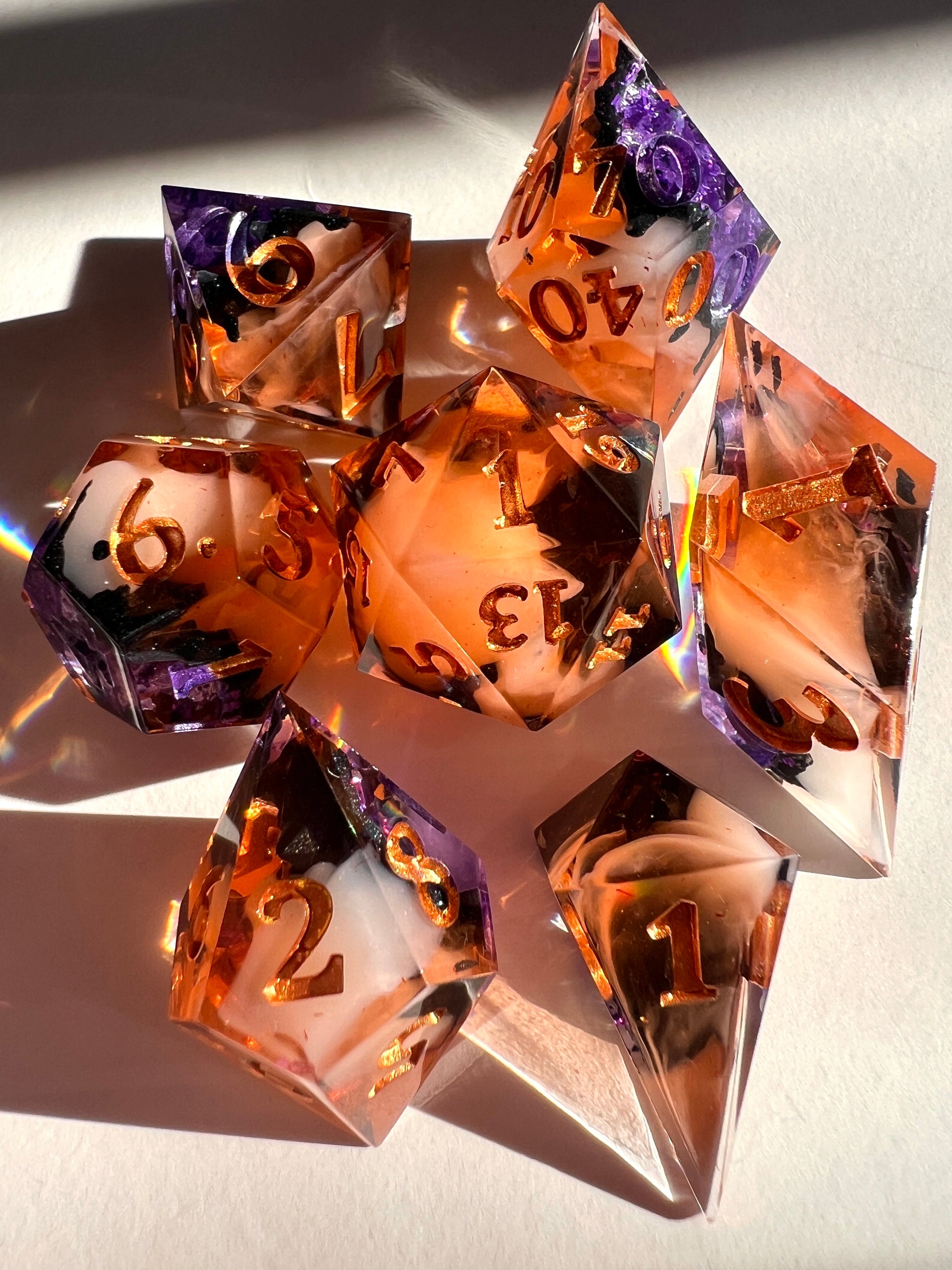 This spooky 7-piece geode-style dice set contains two different shades of purple foil to mimic crystals, a black inky rim, and an orange and cream-colored base.