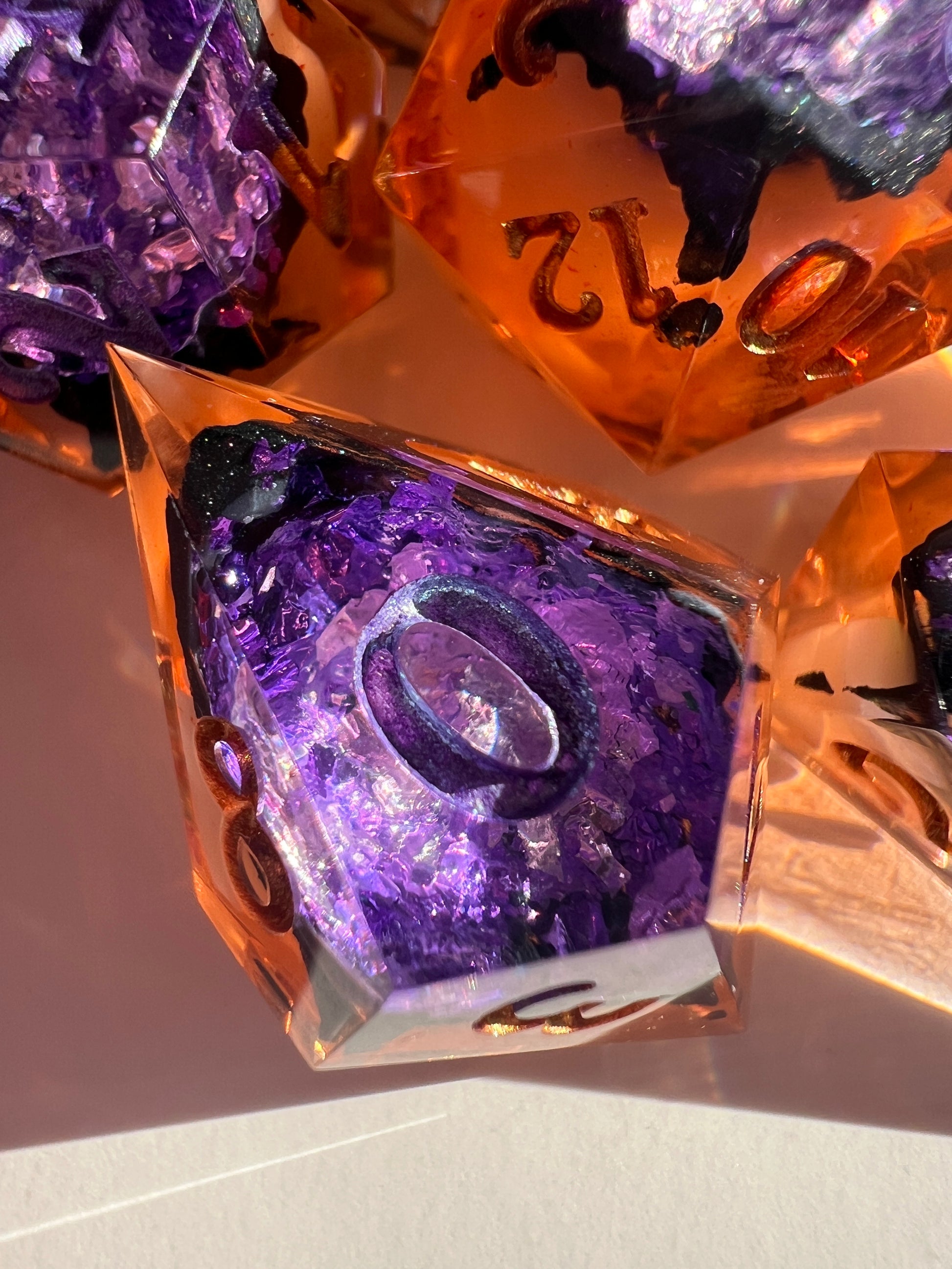 This spooky 7-piece geode-style dice set contains two different shades of purple foil to mimic crystals, a black inky rim, and an orange and cream-colored base.