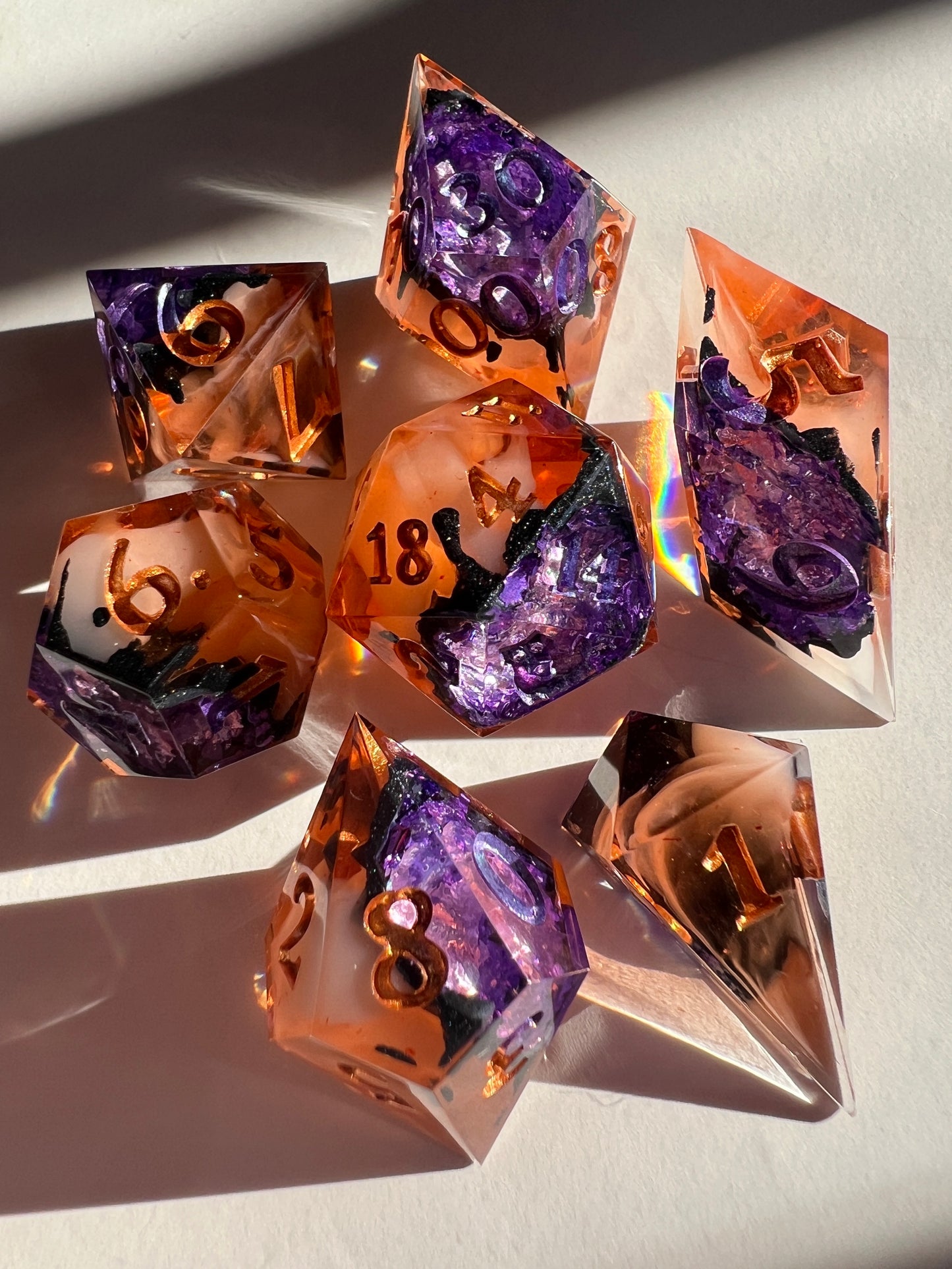 This spooky 7-piece geode-style dice set contains two different shades of purple foil to mimic crystals, a black inky rim, and an orange and cream-colored base.