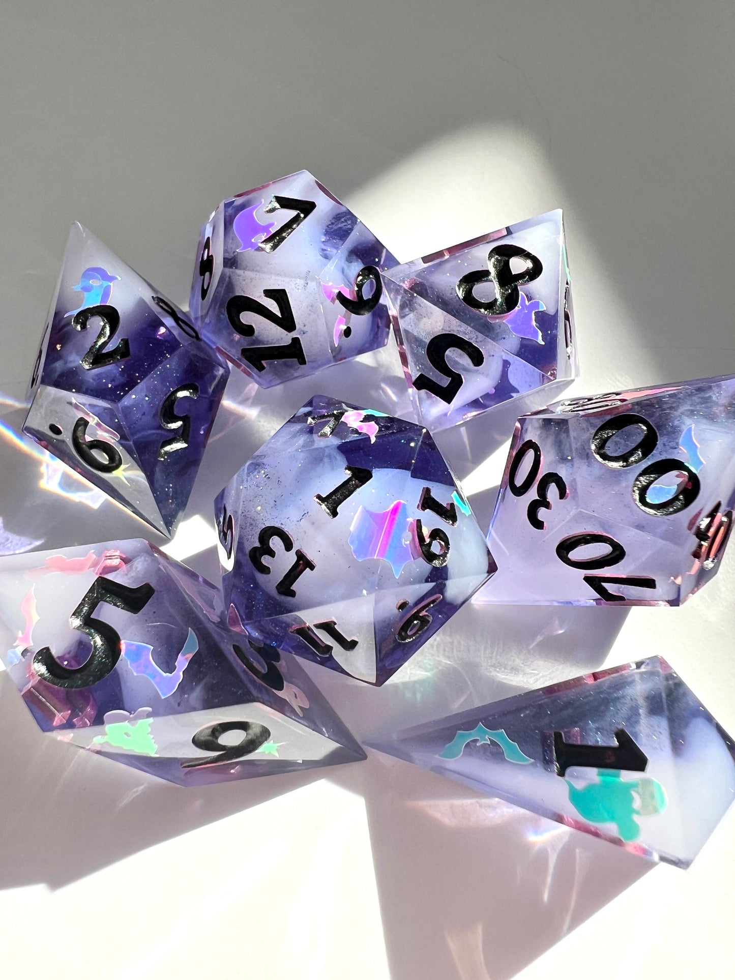 This 7-piece resin set features purple to black gradient dice with cream wisps and holographic bat and ghost decals. 