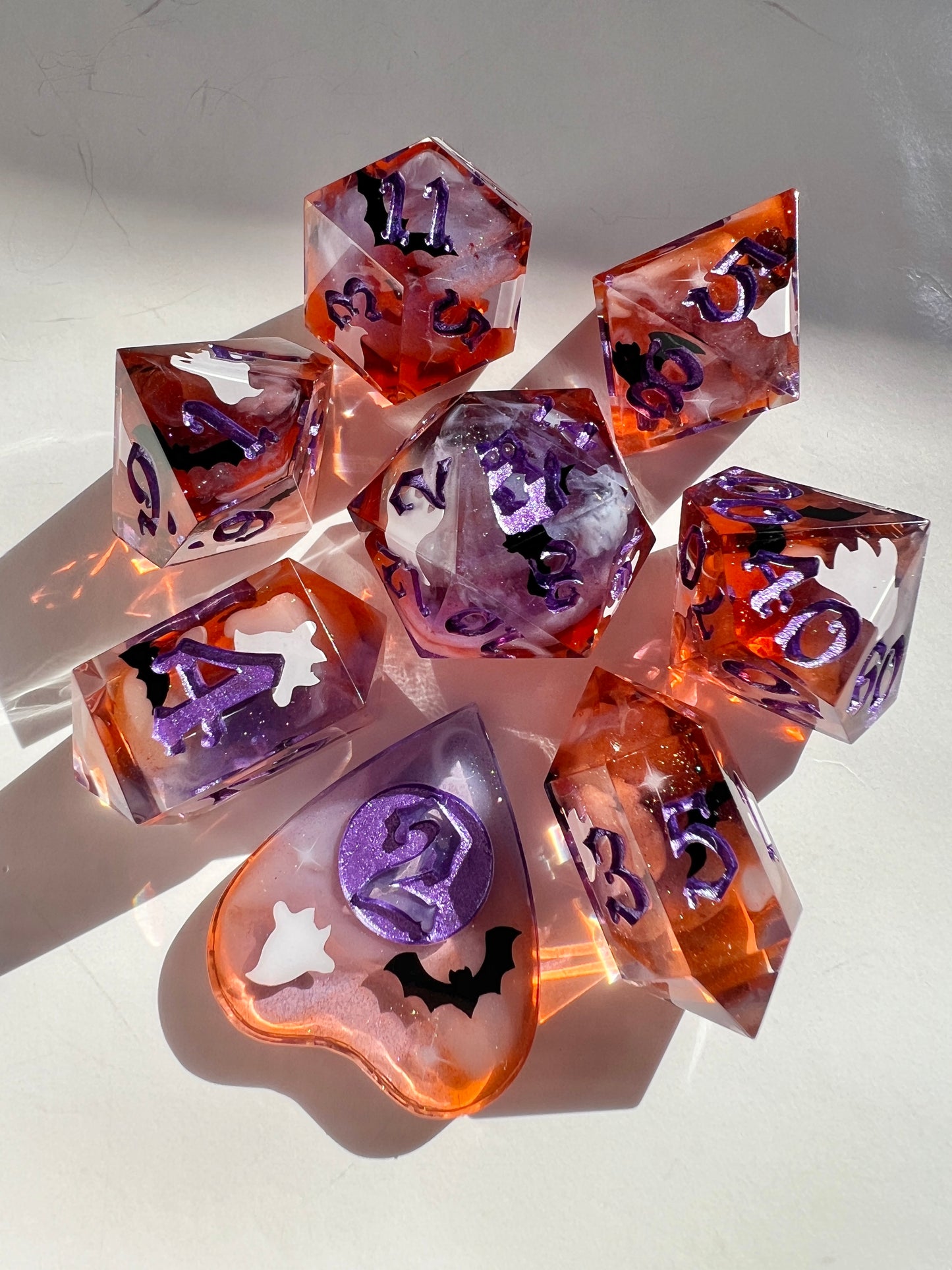 This 8-piece resin dice set features a purple to orange gradient, white wisps, and ghost cat and bat decals. 