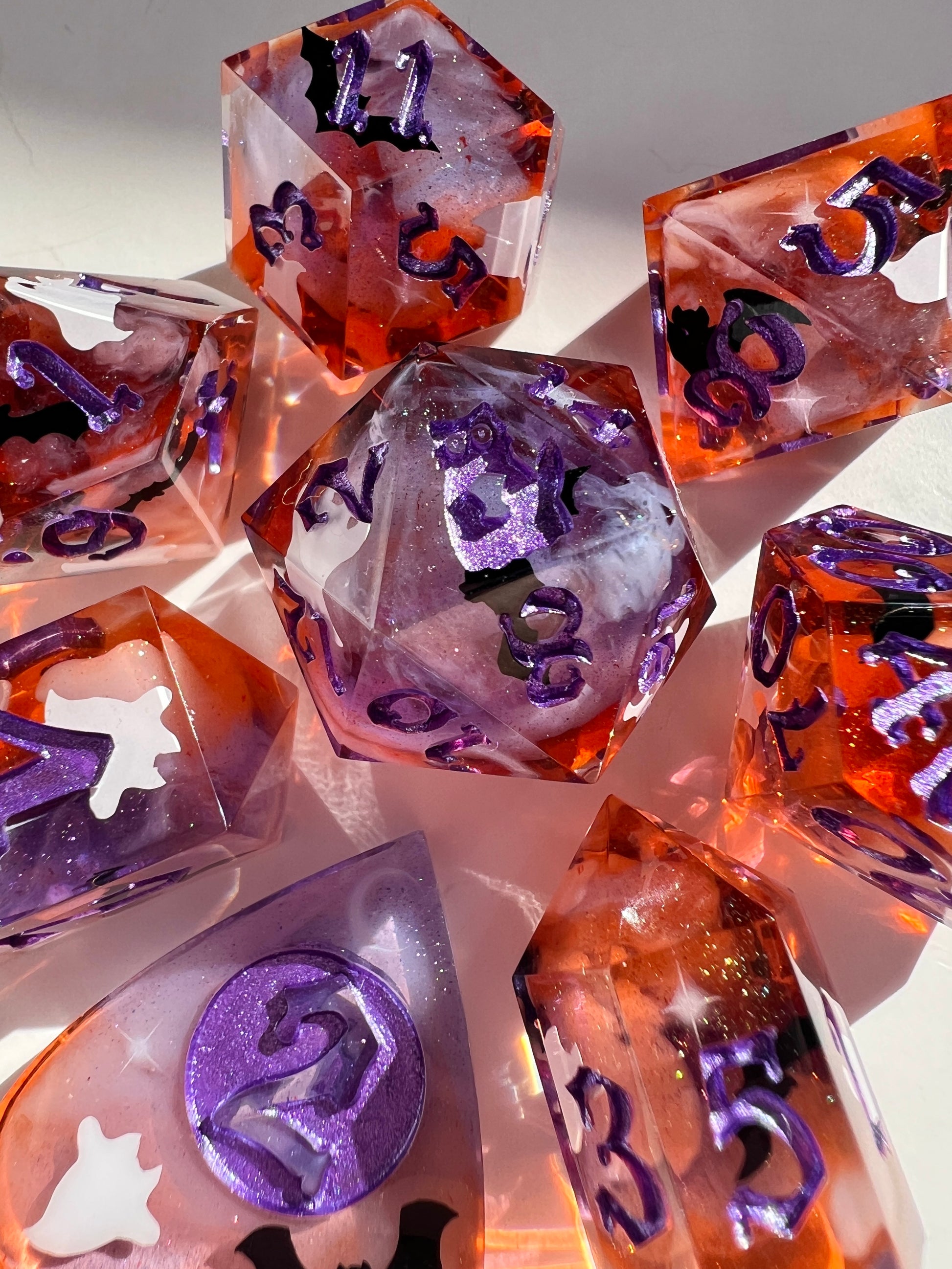 This 8-piece resin dice set features a purple to orange gradient, white wisps, and ghost cat and bat decals. 