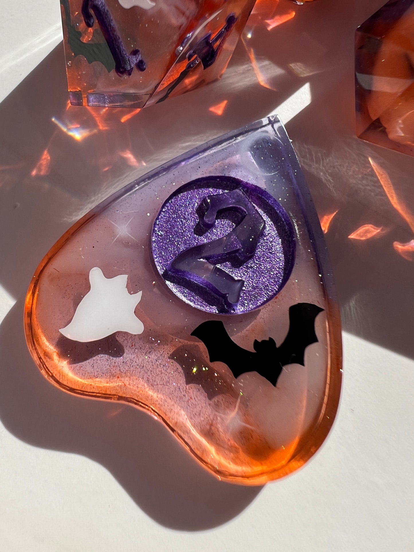 This 8-piece resin dice set features a purple to orange gradient, white wisps, and ghost cat and bat decals. 