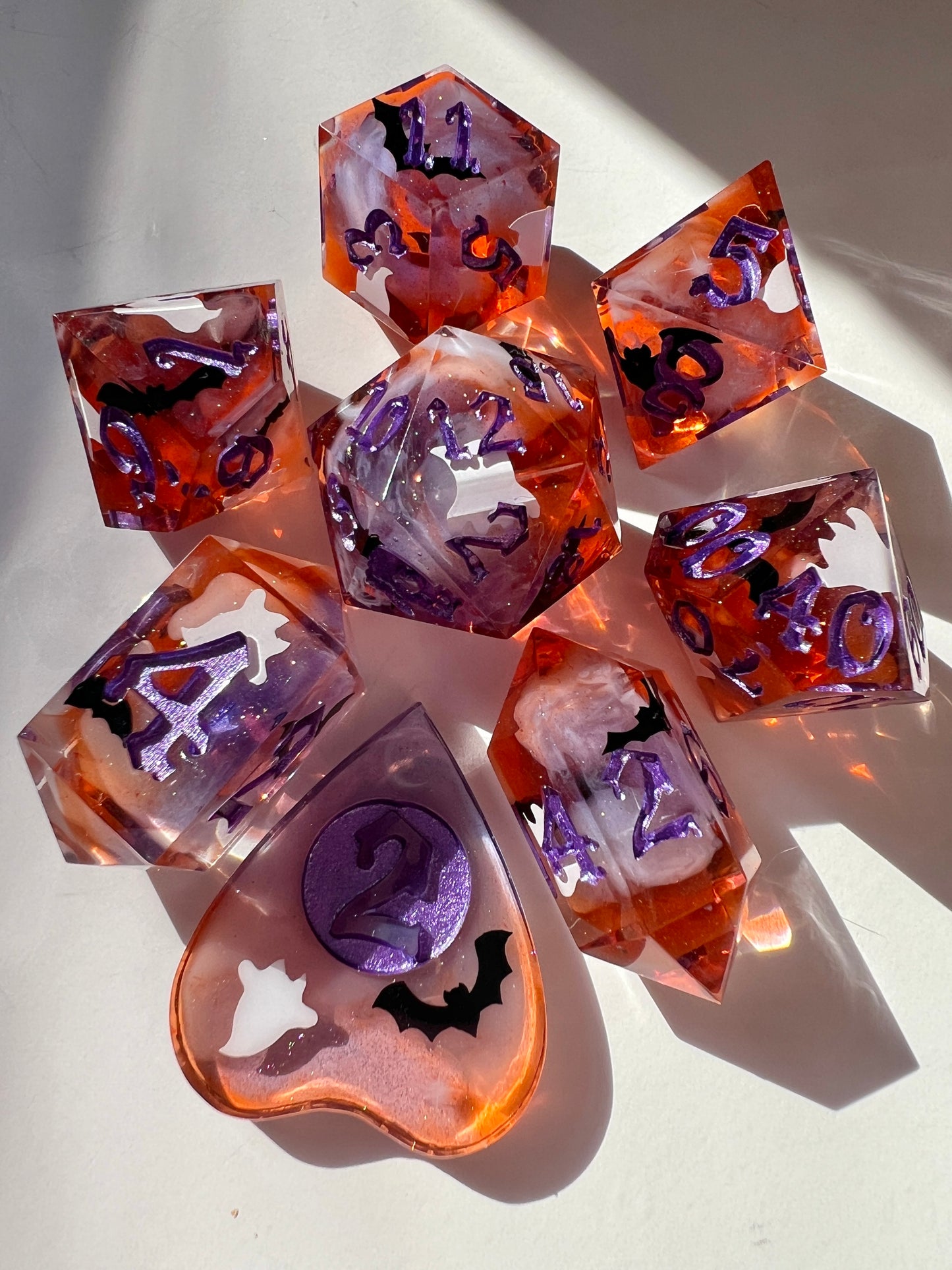 This 8-piece resin dice set features a purple to orange gradient, white wisps, and ghost cat and bat decals. 